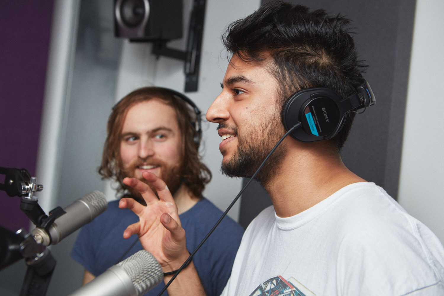 Two young people wearing headphones smiling and recording a podcast