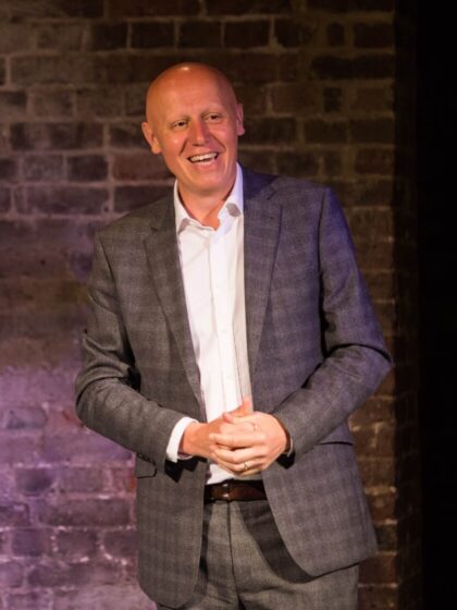 Marcus Davey stands in front of a brick wall whilst talking to a crowd.