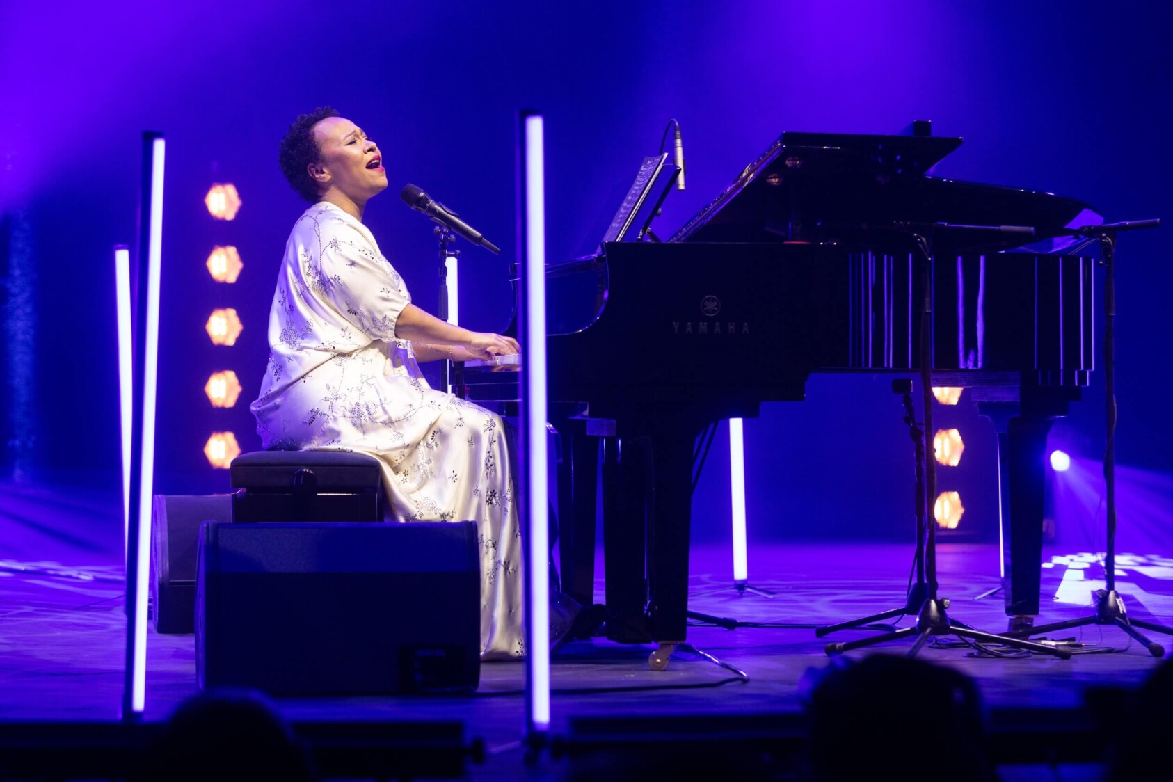 Emeli Sande sits at a piano whilst singing to the crowd.