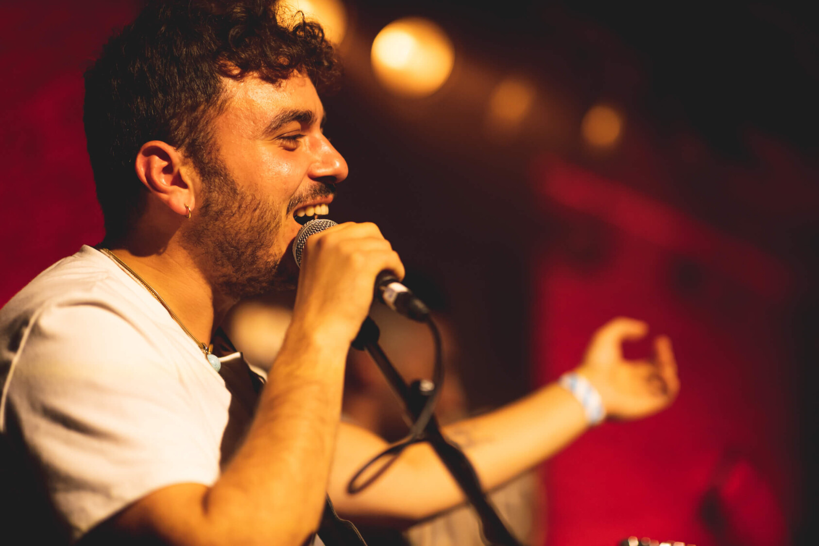 A man smiling and holding a microphone against a dark red backgound