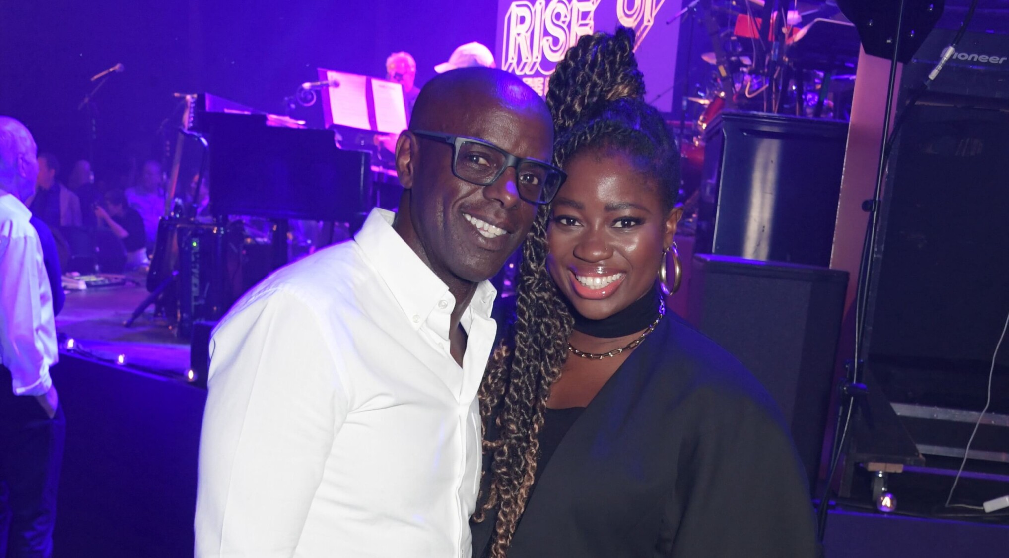 Trevor Nelson and Clara Amfo stand next to each other, smiling to the camera, as they get their photo taken with the main stage in the background.