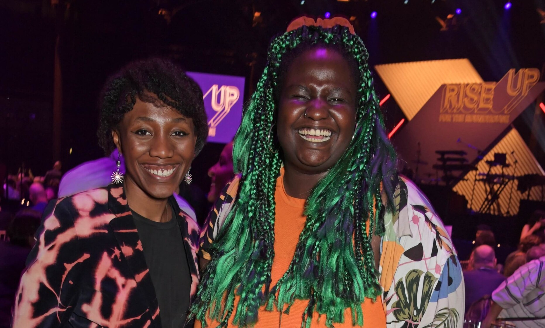 Chisara Agor and Ruth Awolola stand next to each other, smiling to the camera, with the main stage in the background.