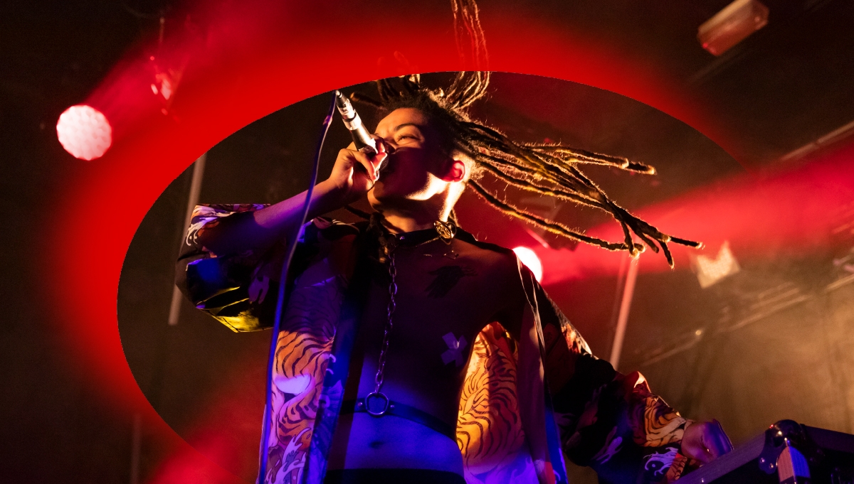 An artist performs on stage at Roundhouse Rising Festival and there is a red crescent graphic over the top of the picture.