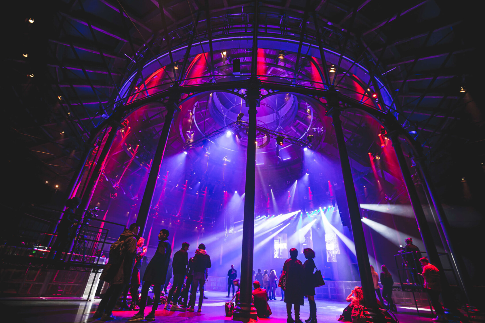 The inside of the auditorium lit up purple, featuring tall steel beams in a circulare shape and people standing between them in silhouette