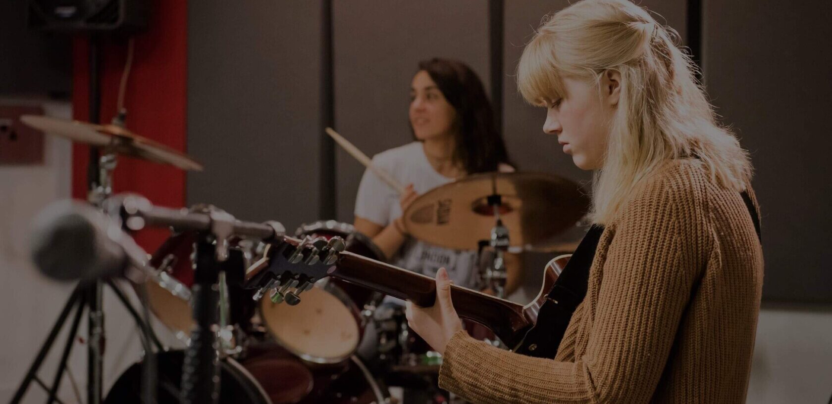 Two young people play the drums and guitar in a rehearsal space in the Roundhouse Studios.