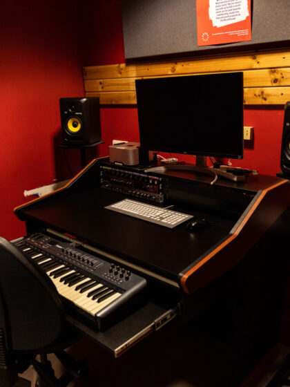 A desk with a keyboard, chair and screen with speakers either side