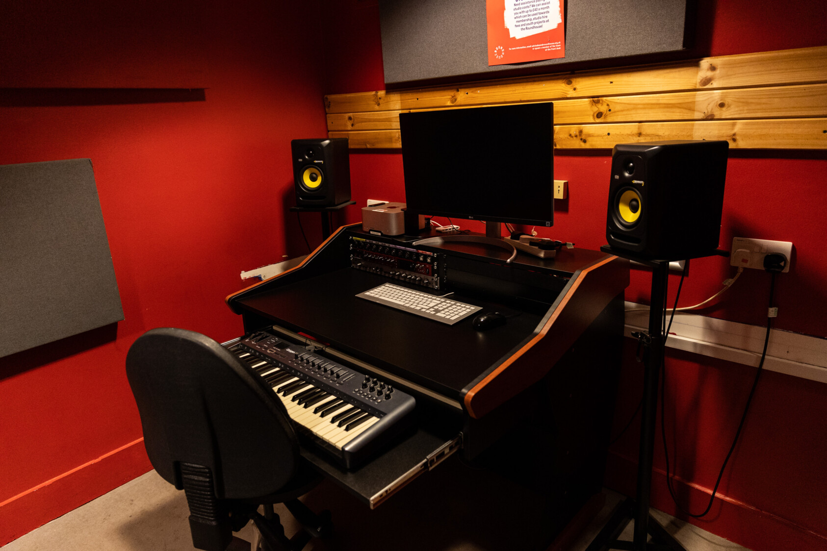 A desk with a keyboard, chair and screen with speakers either side