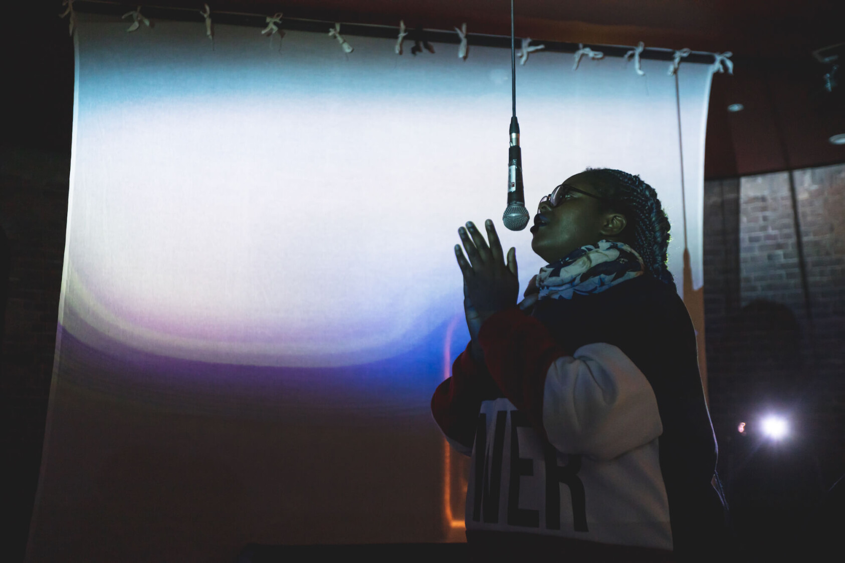 A young person sings into a microphone hanging from the ceiling