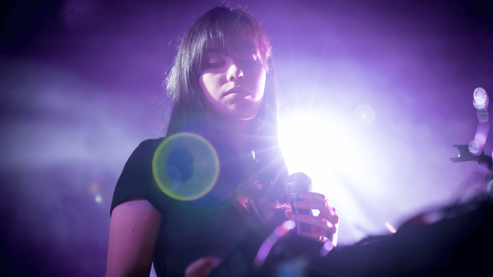 young person holding a mic with bright purple lights behind them