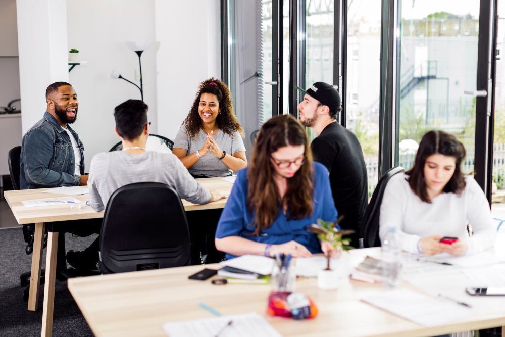 six young people sitting at desks chatting and working