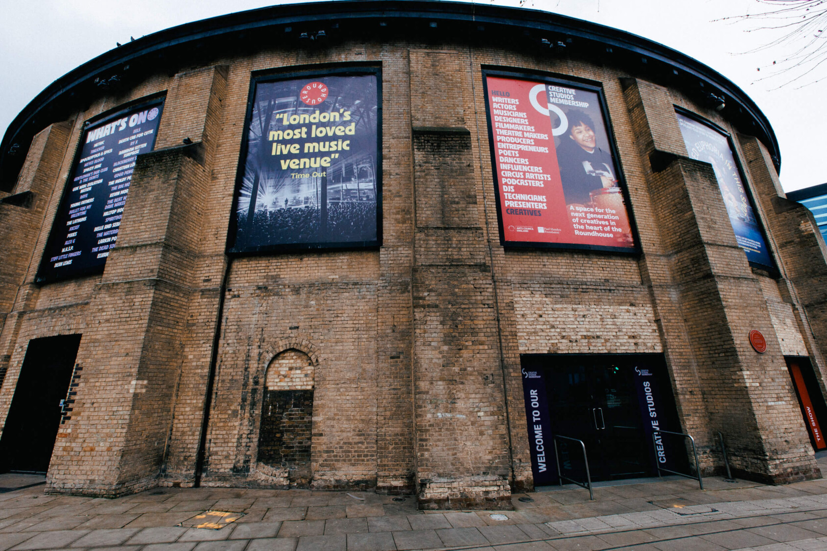 The brick exterior of the Roundhouse with signs on the outside one of which says 'London's most lvoed music venue'