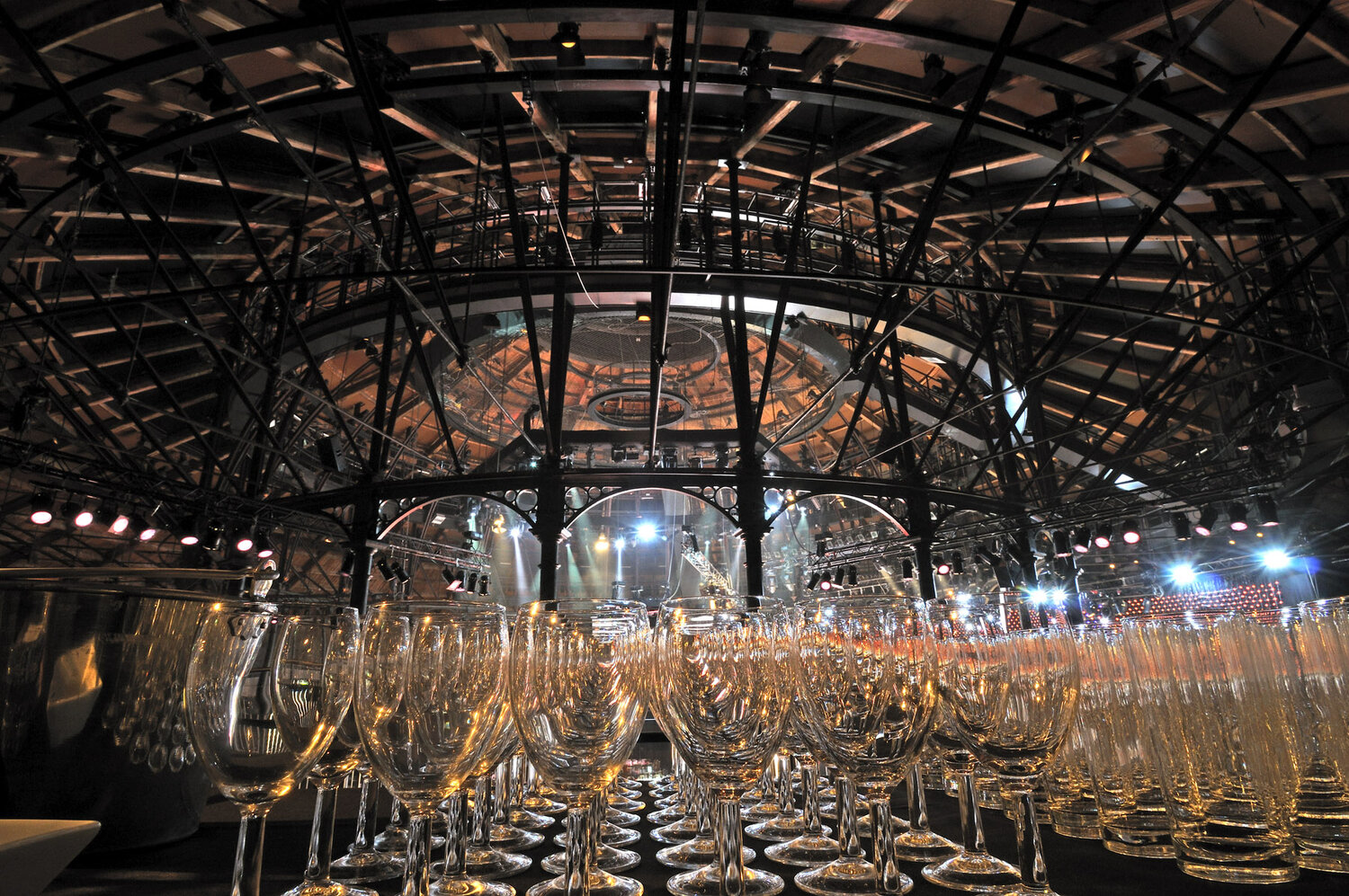 Wine glasses lined up against the ceiling and steel beams of the circular main space