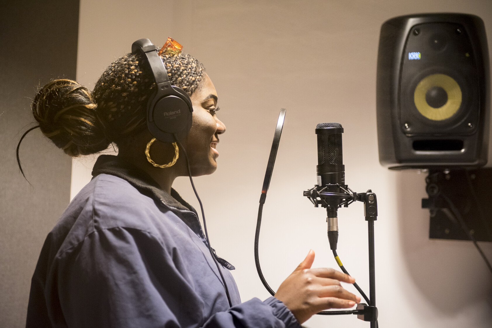 A young woman smiles and speaks into a recording microphone