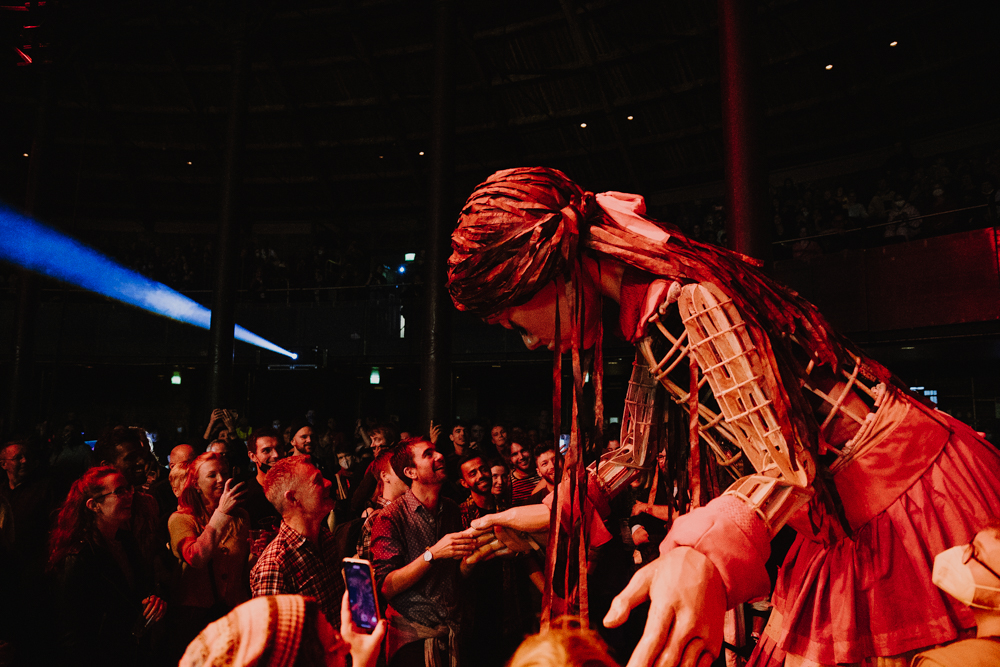 Photo of Little Amal meeting people in a crowd at the Roundhouse. Little Amal is the 12 foot puppet of a 10 year old Syrian refugee child.