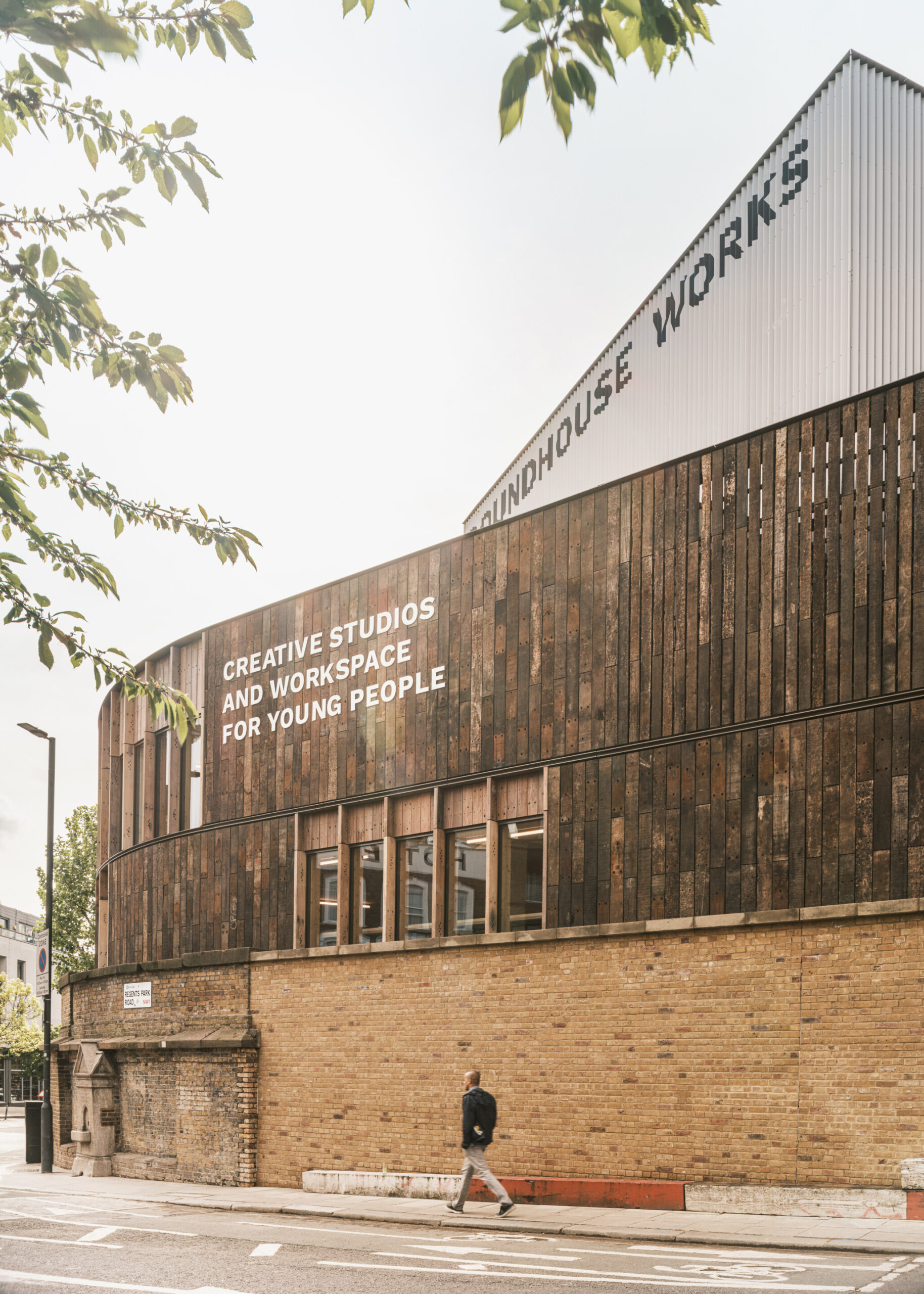 The outside of Roundhouse Works which includes an exposed brick wall, wooden cladding and a metal structure with a person walking in front.