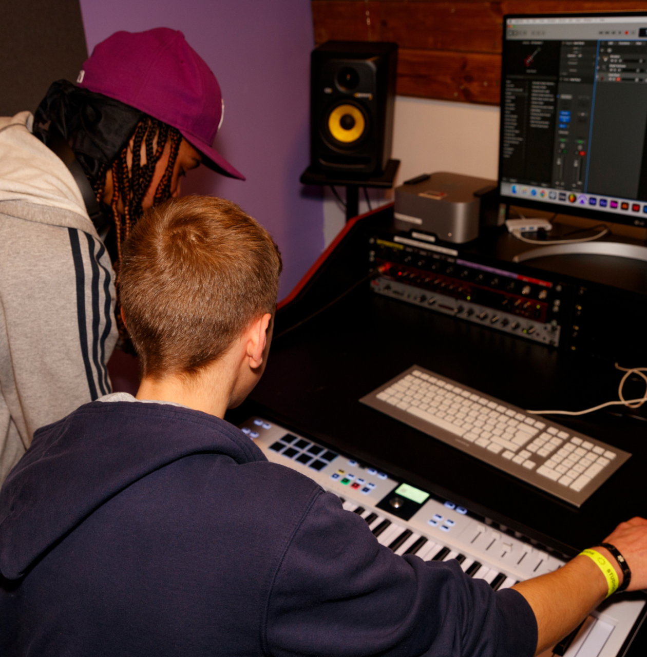 two young people looking at a keyboard and computer producing music