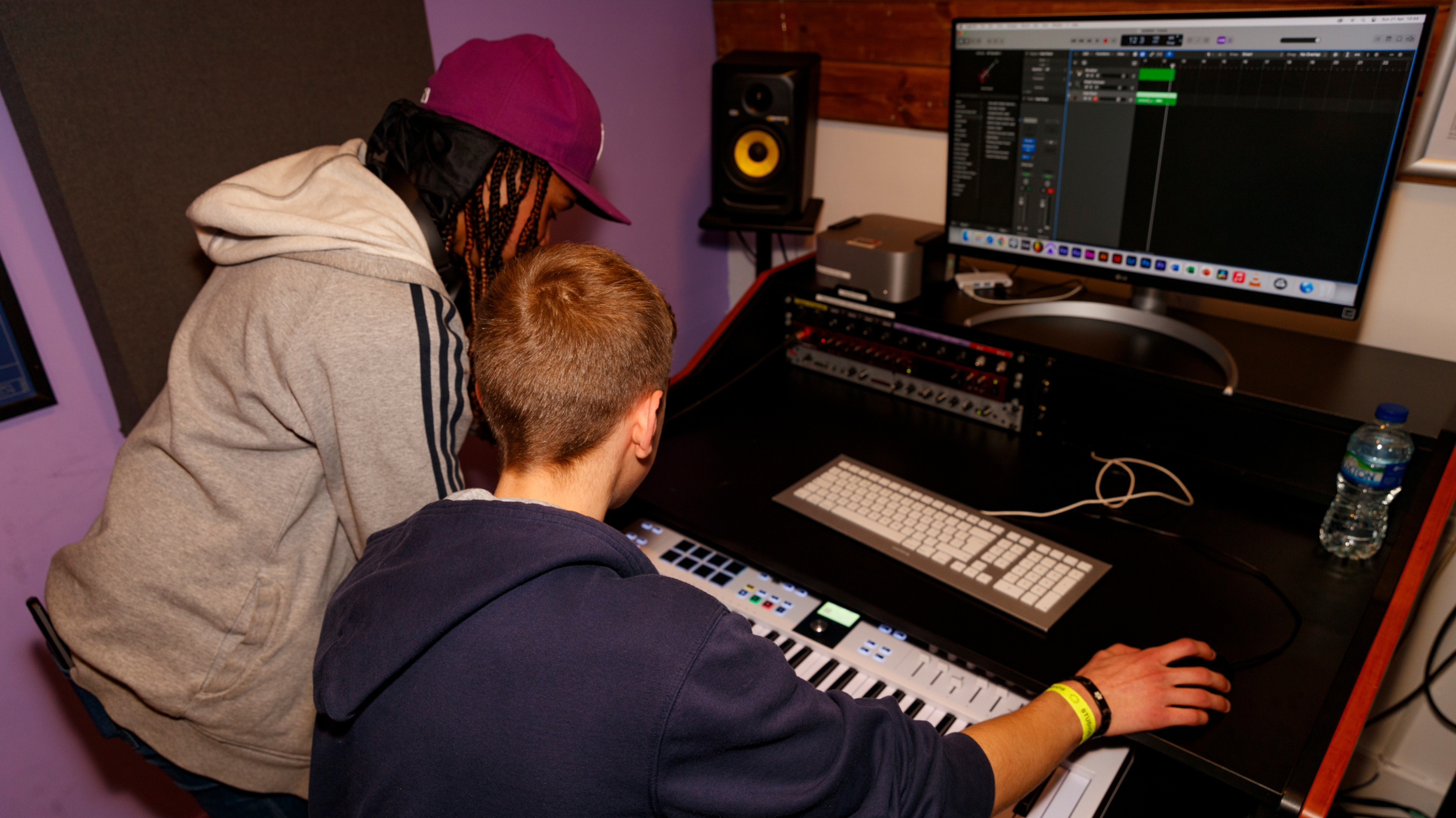 two young people looking at a keyboard and computer producing music