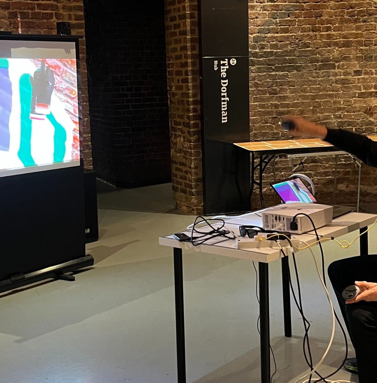 a man sat down wearing a VR head set, pointing at a screen in front of him with graffiti drawn on it
