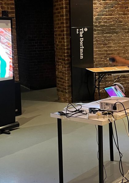 a man sat down wearing a VR head set, pointing at a screen in front of him with graffiti drawn on it