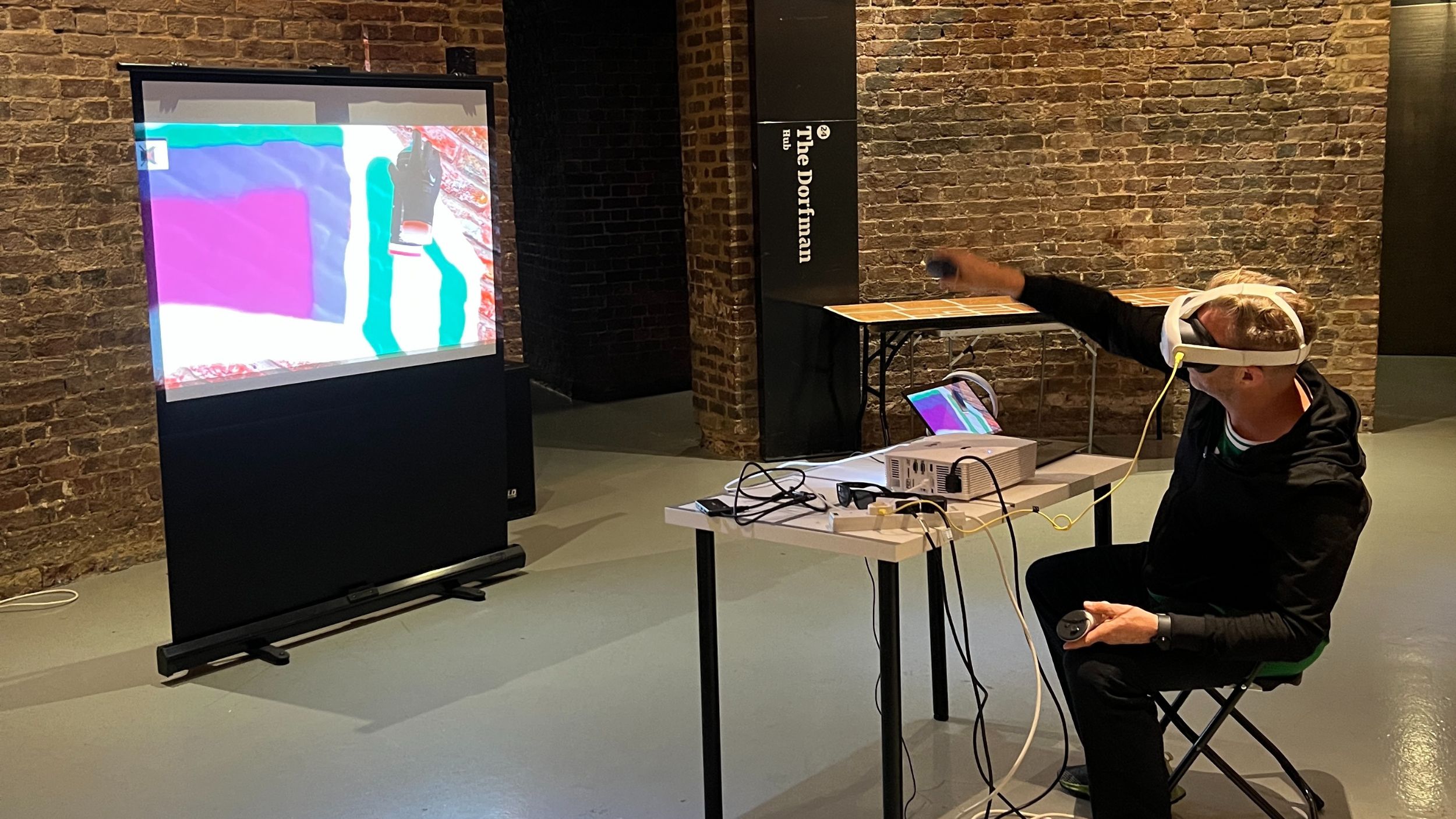 a man sat down wearing a VR head set, pointing at a screen in front of him with graffiti drawn on it