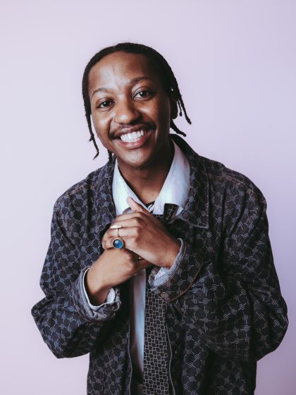 young person with dark skin, braids, wearing a gingham jacket and white shirt