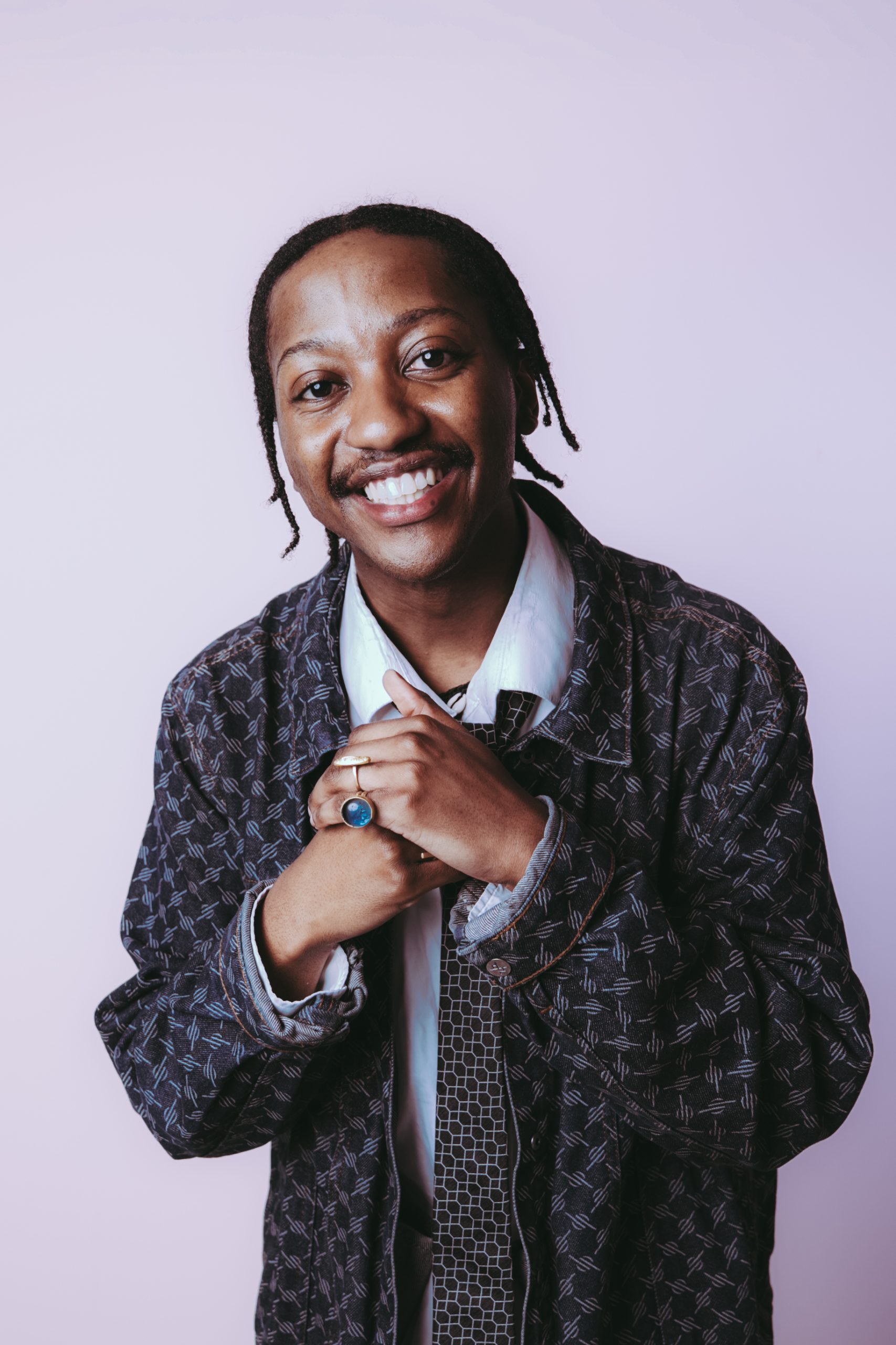 young person with dark skin, braids, wearing a gingham jacket and white shirt