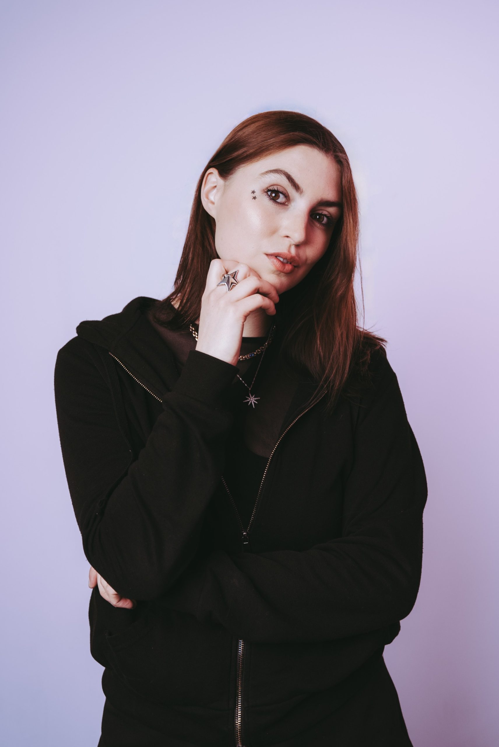Young person with pale skin, long brunette hair wearing a black hoodie