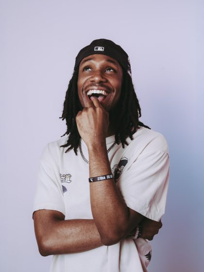 Young person with dark skin and locks, wearing a backwards cap and white tshirt