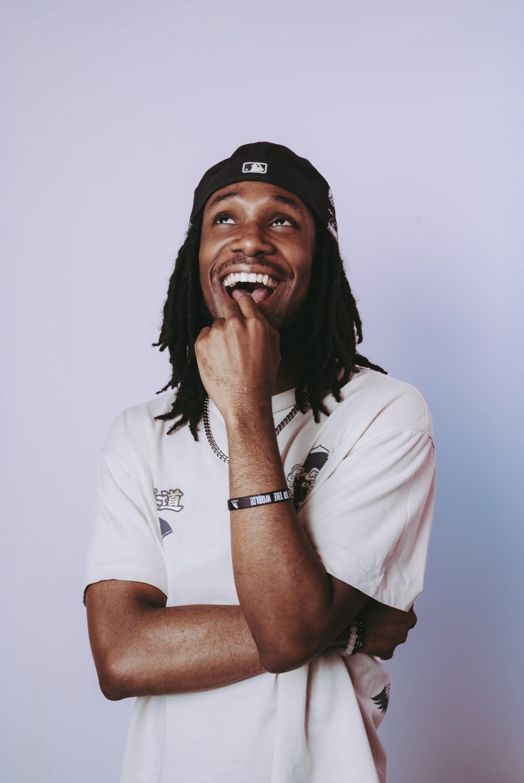 Young person with dark skin and locks, wearing a backwards cap and white tshirt
