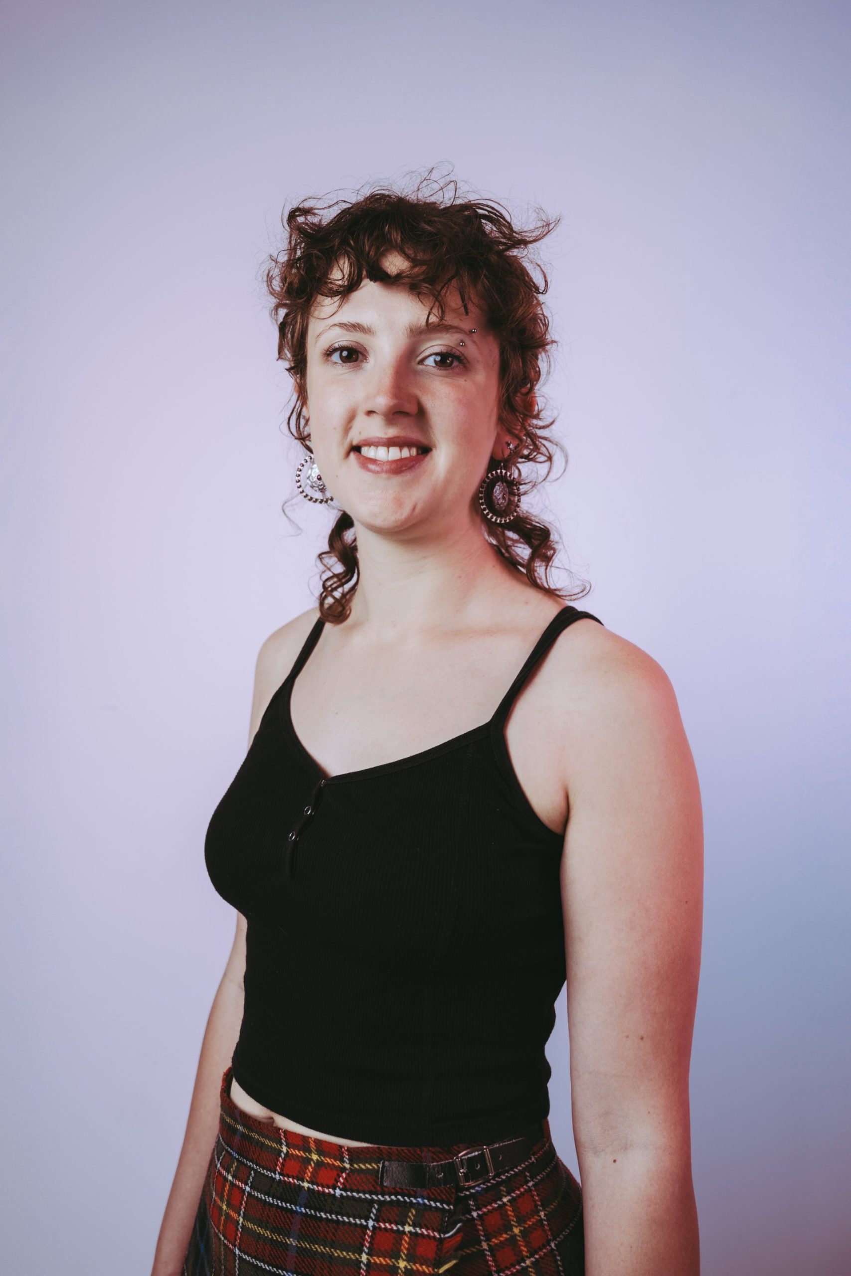 young person with pale skin, short curly brown hair wearing a black vest top