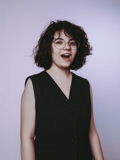 young person with short dark hair and glasses wearing a sleeveless black vest,