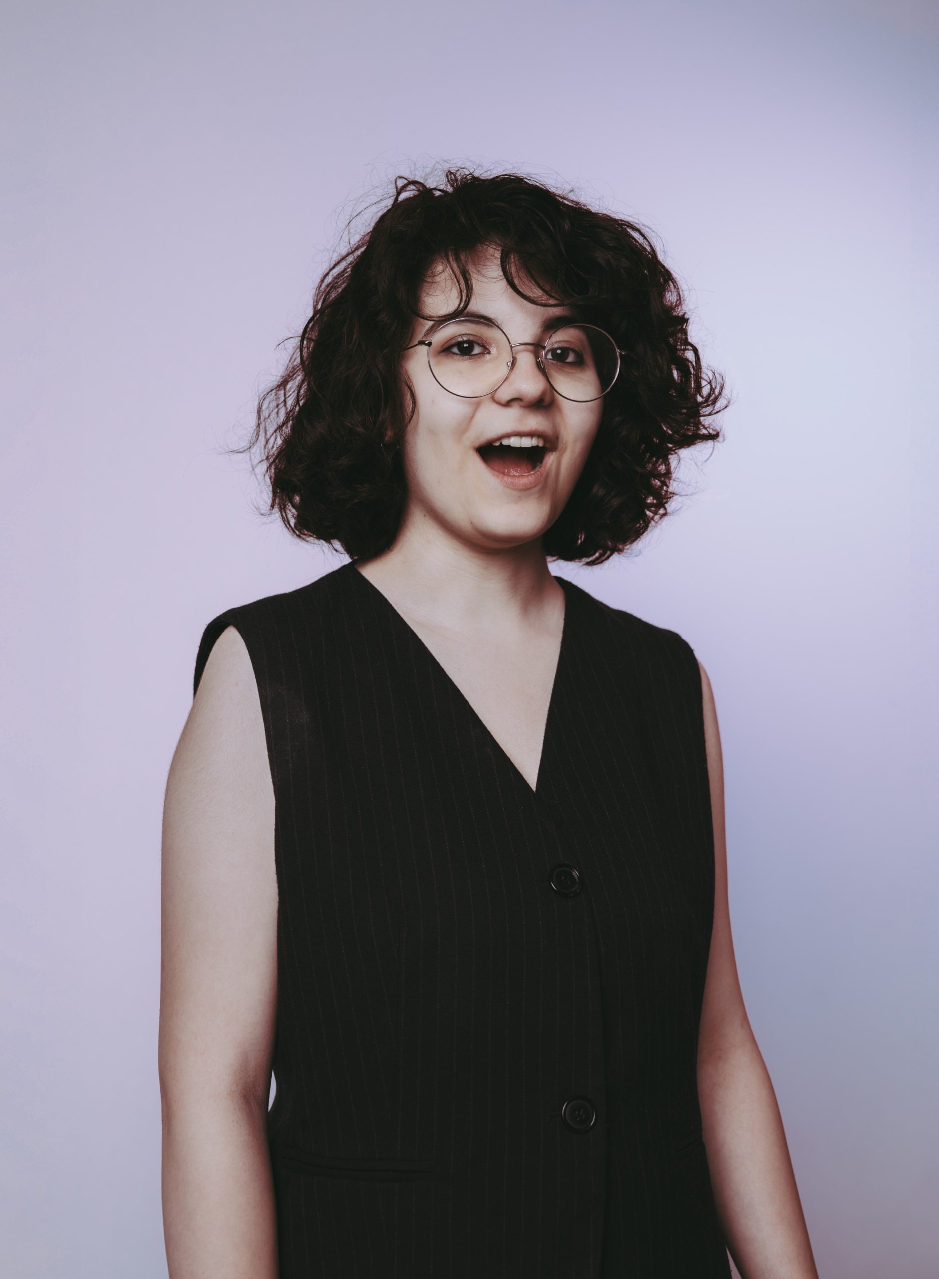 young person with short dark hair and glasses wearing a sleeveless black vest,