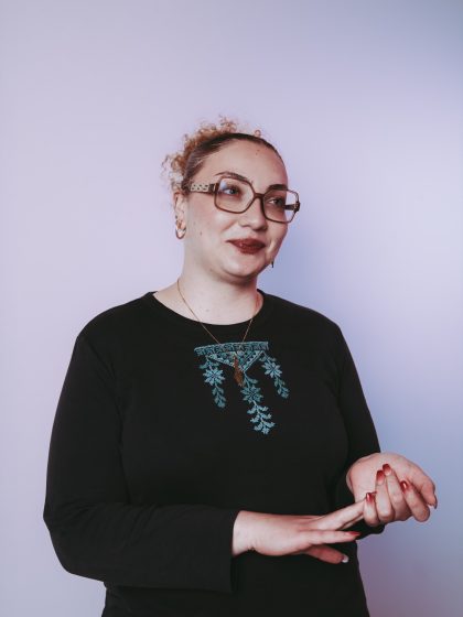 Young person with light skin, glasses and curly hair wearing a black long sleeve top