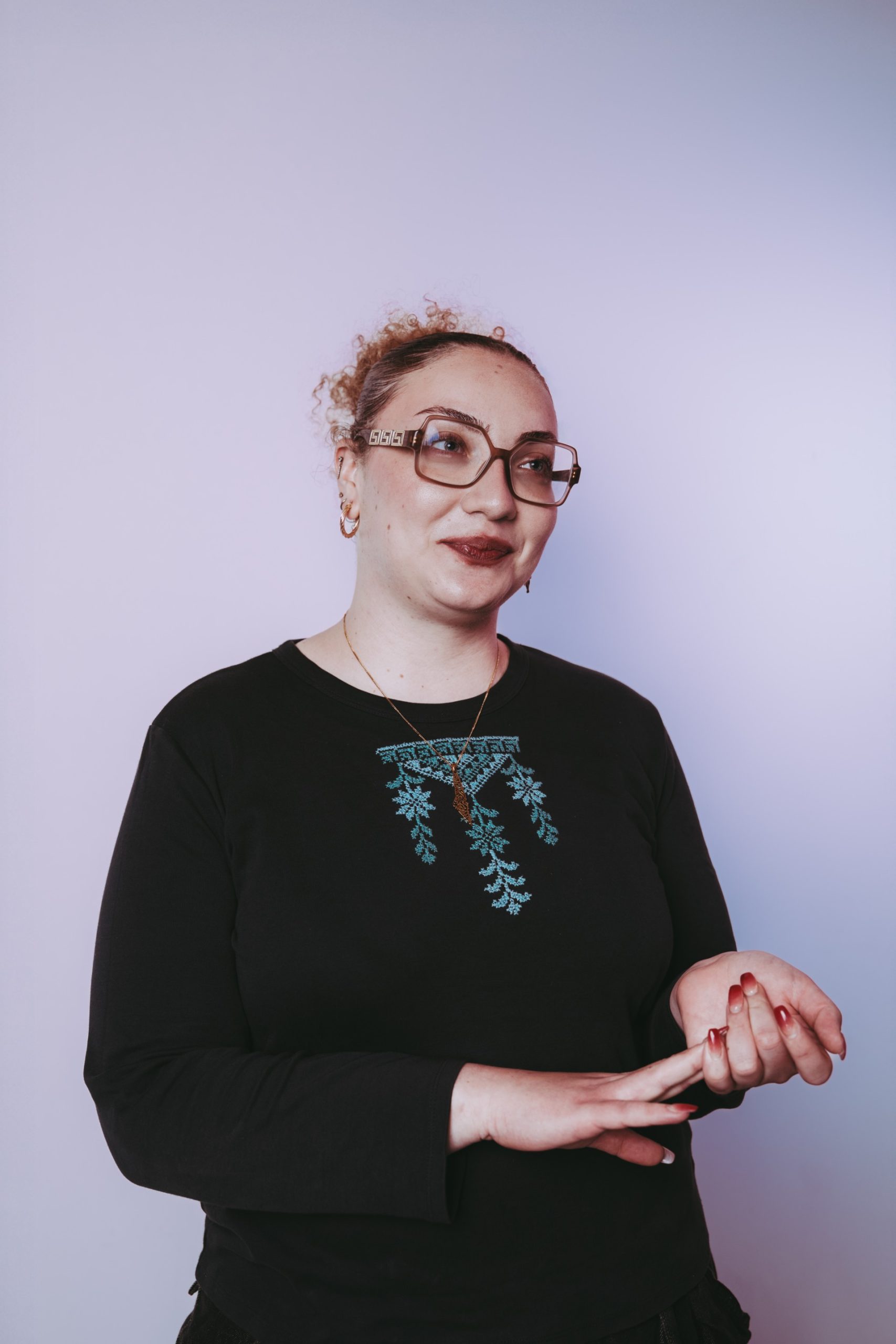Young person with light skin, glasses and curly hair wearing a black long sleeve top