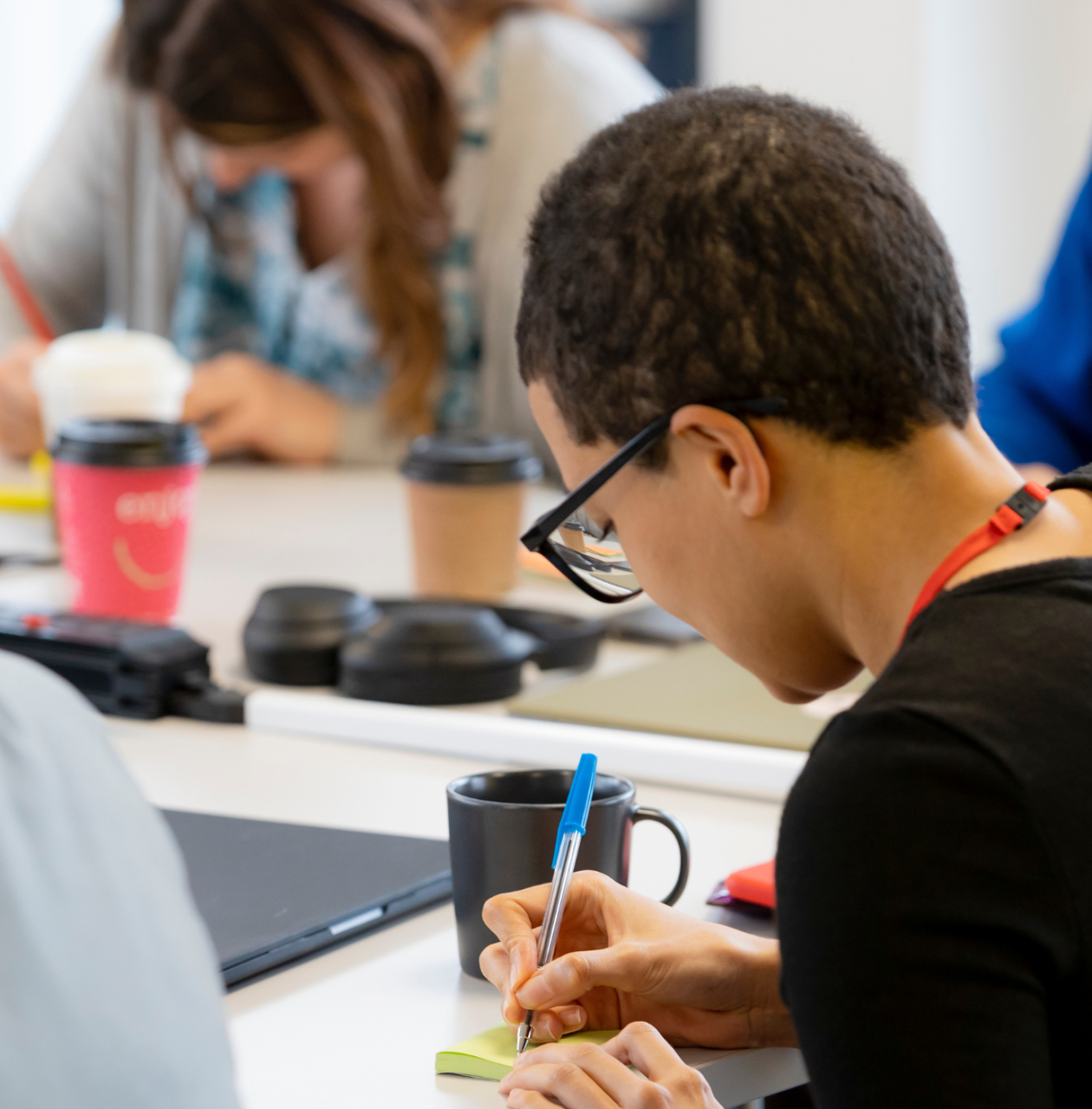 picture showing a young person writing their ideas on a sticky note, surrounded by others doing the same
