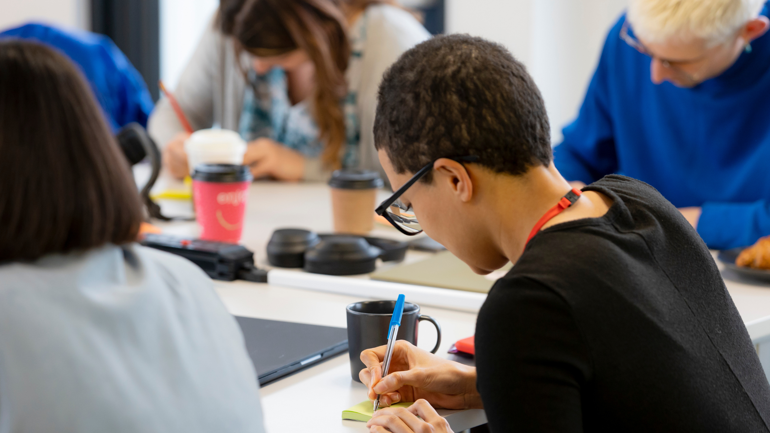 picture showing a young person writing their ideas on a sticky note, surrounded by others doing the same