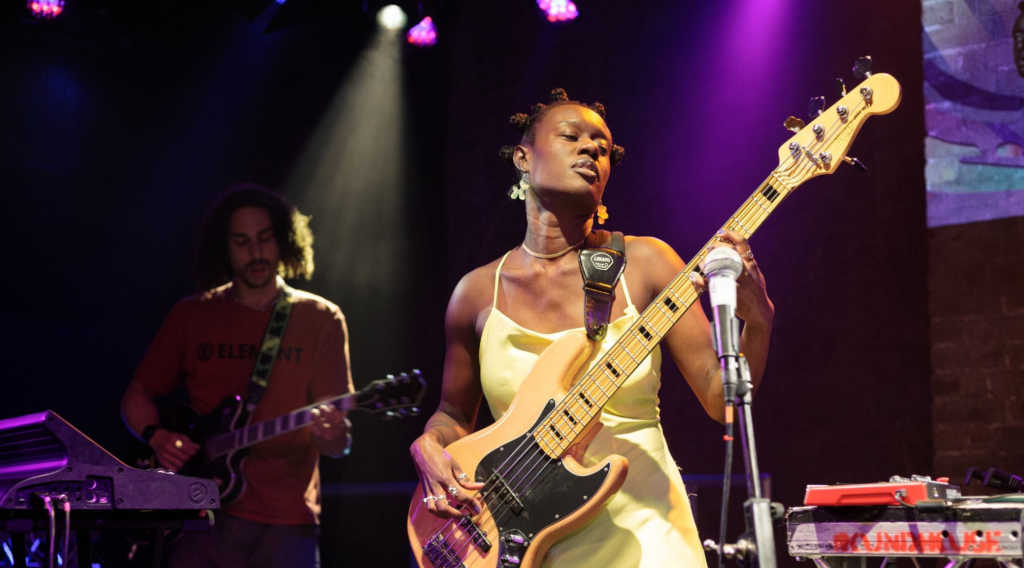 Marla is wearing a pale yellow silk dress, playing bass on stage