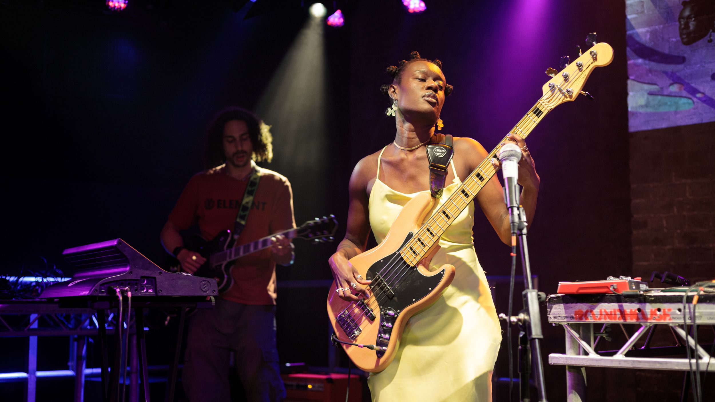 Marla is wearing a pale yellow silk dress, playing bass on stage