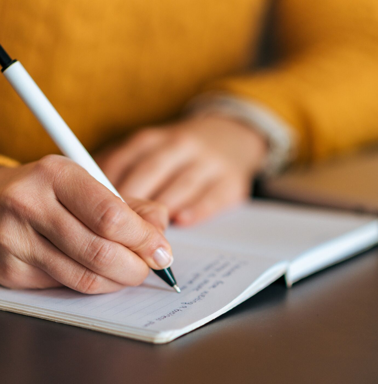 A zoomed in photo of a hand writing with a pen in a notebook
