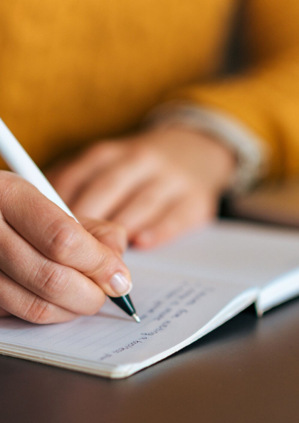 A zoomed in photo of a hand writing with a pen in a notebook