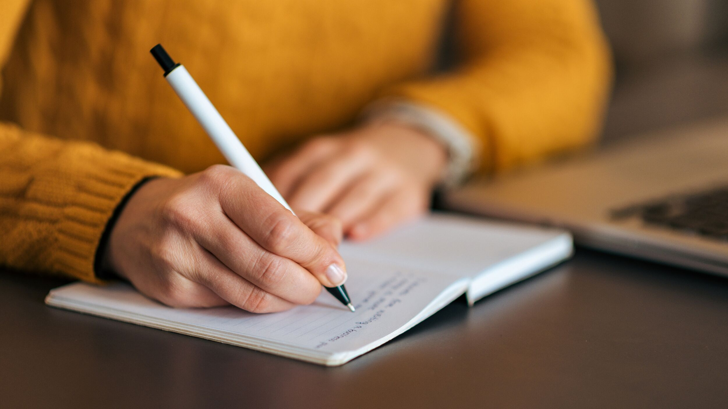 A zoomed in photo of a hand writing with a pen in a notebook