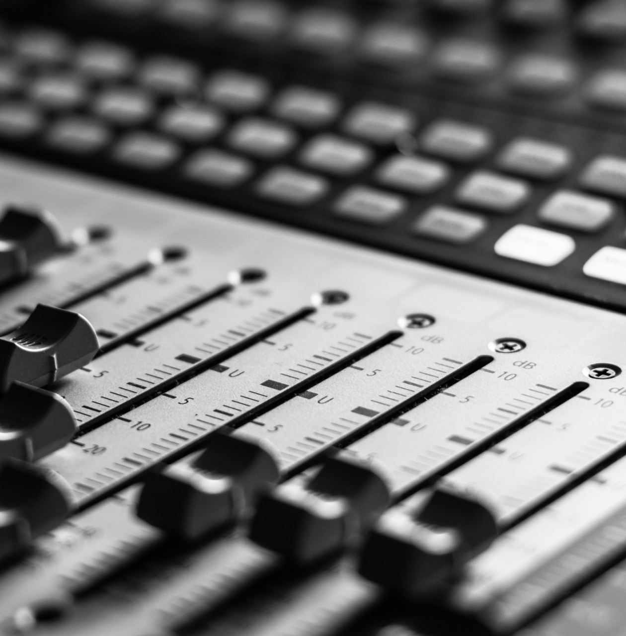Close-up of an audio mixing console with sliders and buttons.