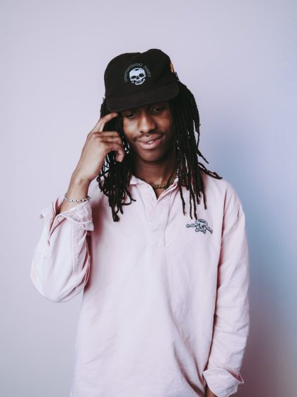 young person with dark skin and locks wearing a white shirt and dark cap