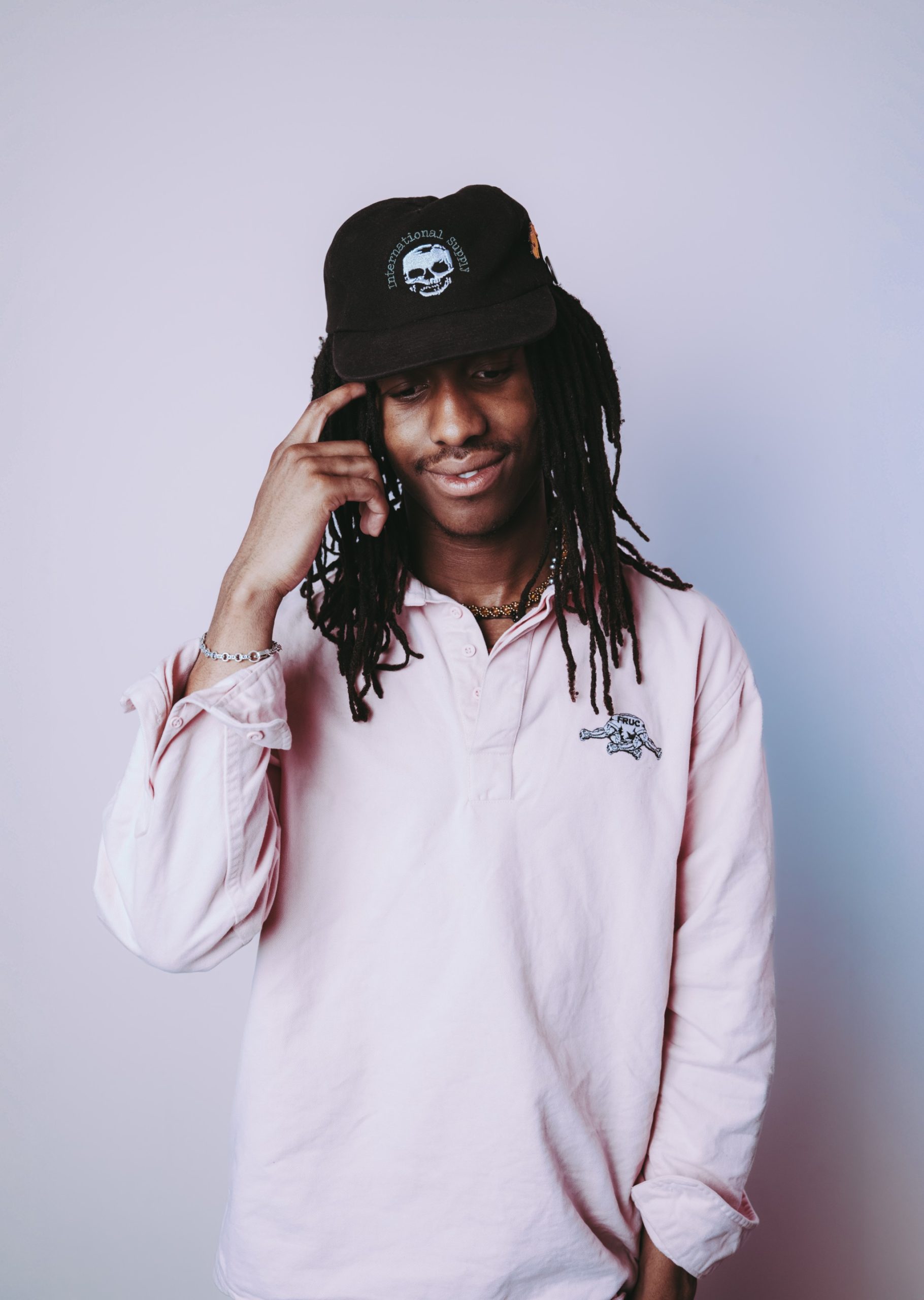 young person with dark skin and locks wearing a white shirt and dark cap