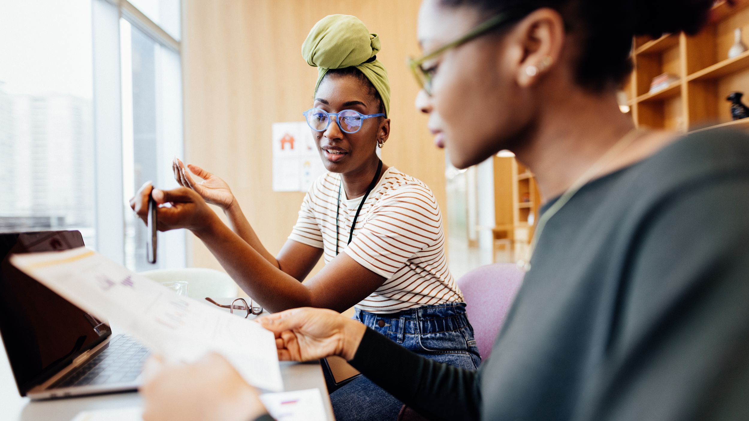 Two people, one wearing glasses, look together at a computer screen or document in an office setting.