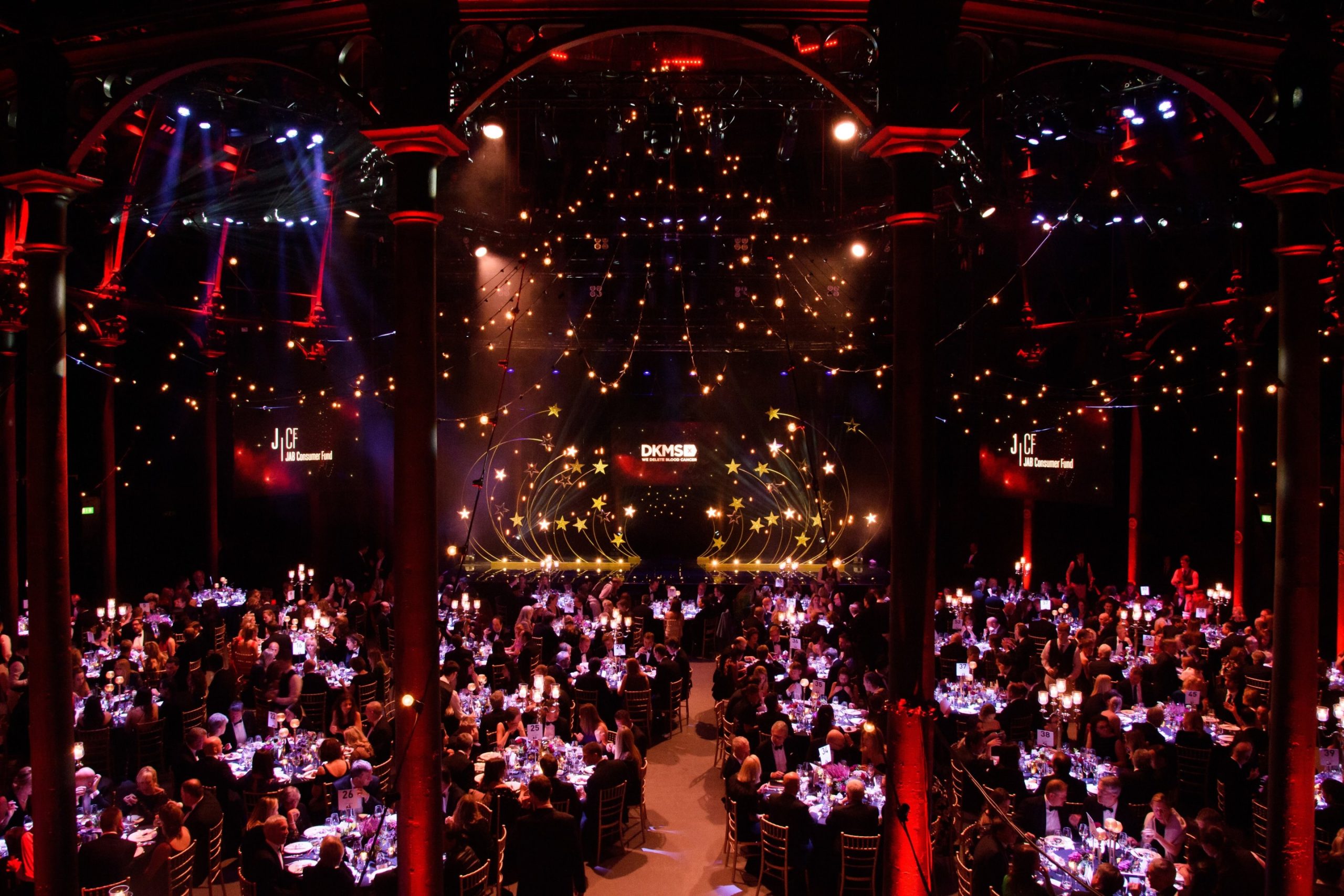 The interior of the Roundhouse is filled with small round tables with guests sitting around them. The lighting is low and red and it has the feel of a fancy event.