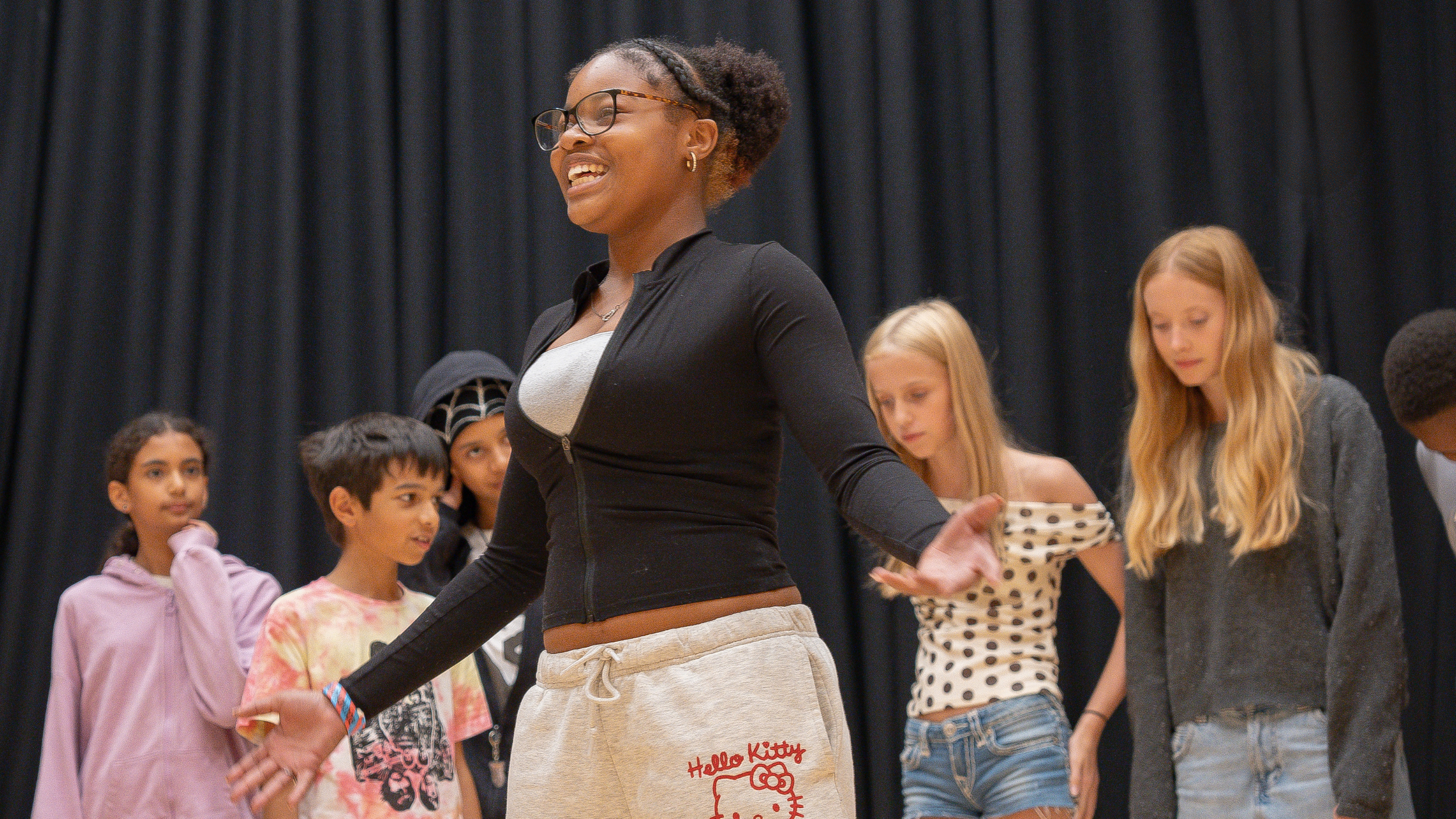 a group of 6 young people performing smiling, against a black curtain in the backdrop